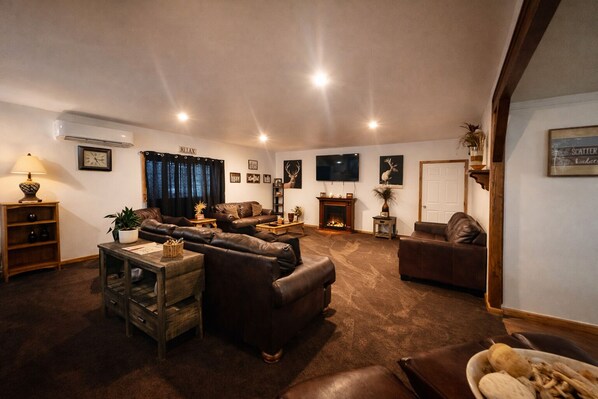 A cozy living room with leather sofas, a fireplace, a television, and a bookshelf.