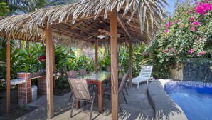 Ein überdachter Außenbereich mit Pool, umgeben von üppiger Vegetation und blühenden Pflanzen.