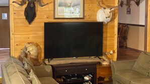 A living room with a large flat-screen TV, wooden walls, mounted animal heads, and a framed picture.