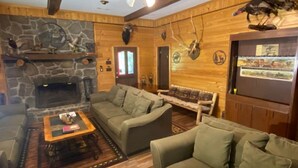 A cozy cabin interior with a stone fireplace, wooden walls, and a ceiling fan.