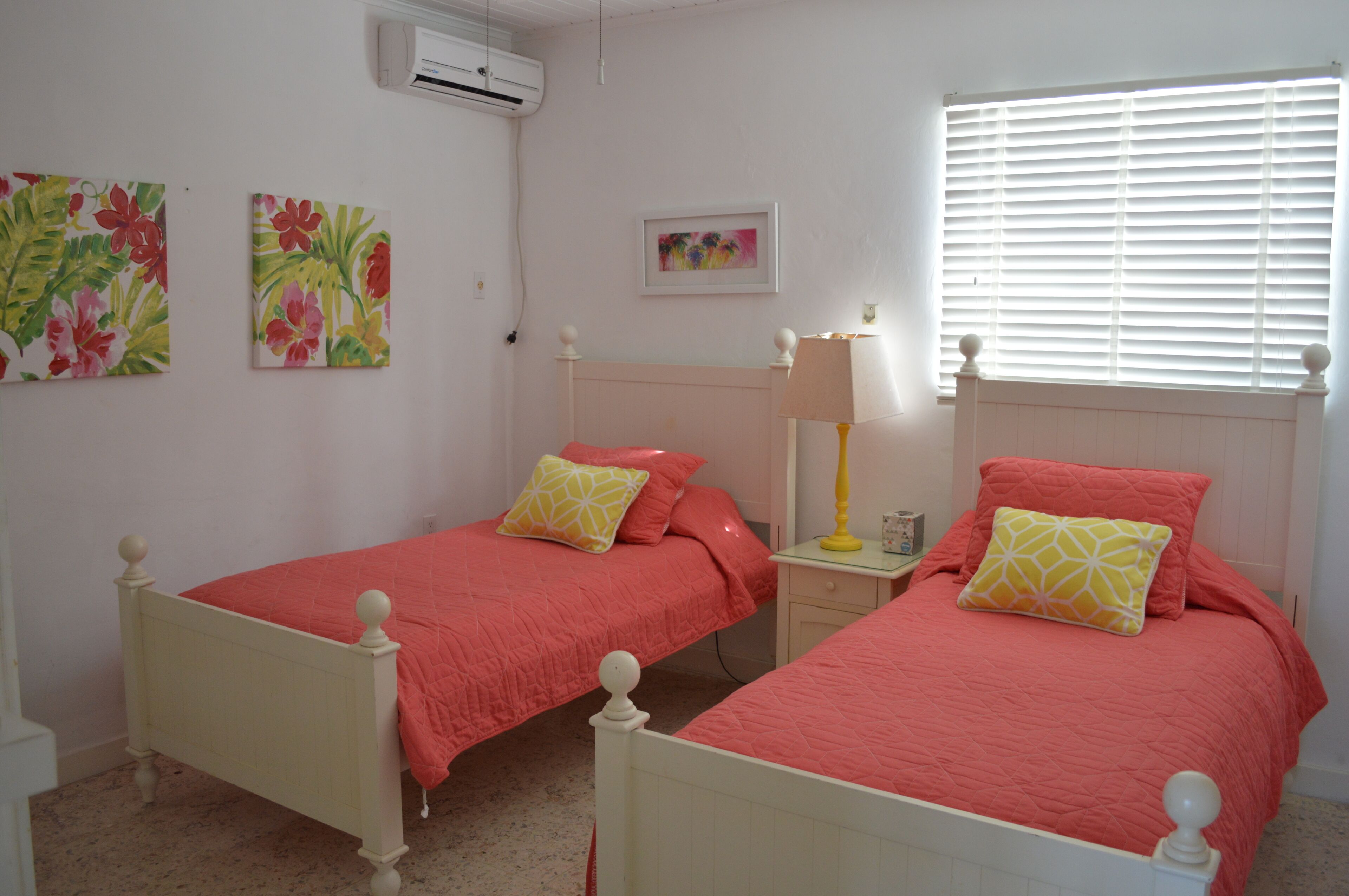 A bedroom with two single beds, a nightstand with a lamp, and wall art.