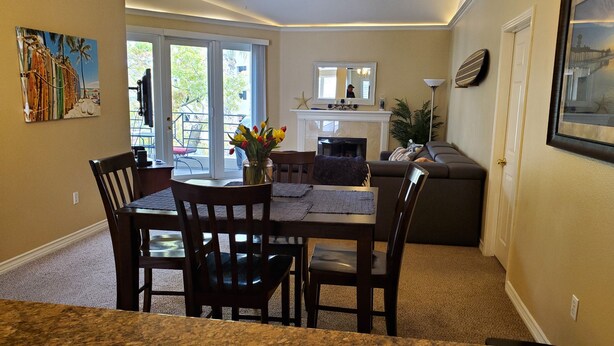 A dining area with a table and chairs, a vase with flowers, and a view of the outdoors through a glass door. - Penthouse - Resort living (Irvine)