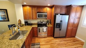A kitchen with wooden cabinets, granite countertops, stainless steel appliances, and a granite backsplash. - Penthouse - Resort living (Irvine)