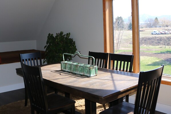 Enjoy meals in this dining area with a table and chairs, surrounded by a scenic view of a grassy field and distant mountains.