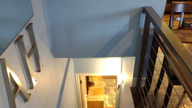 A carpeted staircase with a metal handrail leading to a room with patterned tiles.