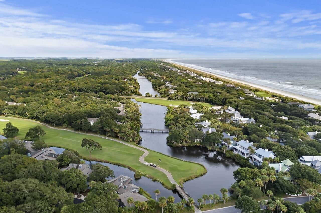 An aerial view of a coastal area with a golf course, a river, and beachfront properties.