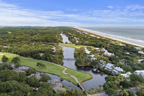 Luftaufnahme einer Küstenregion mit einem Golfplatz, einem Fluss und Strandimmobilien.