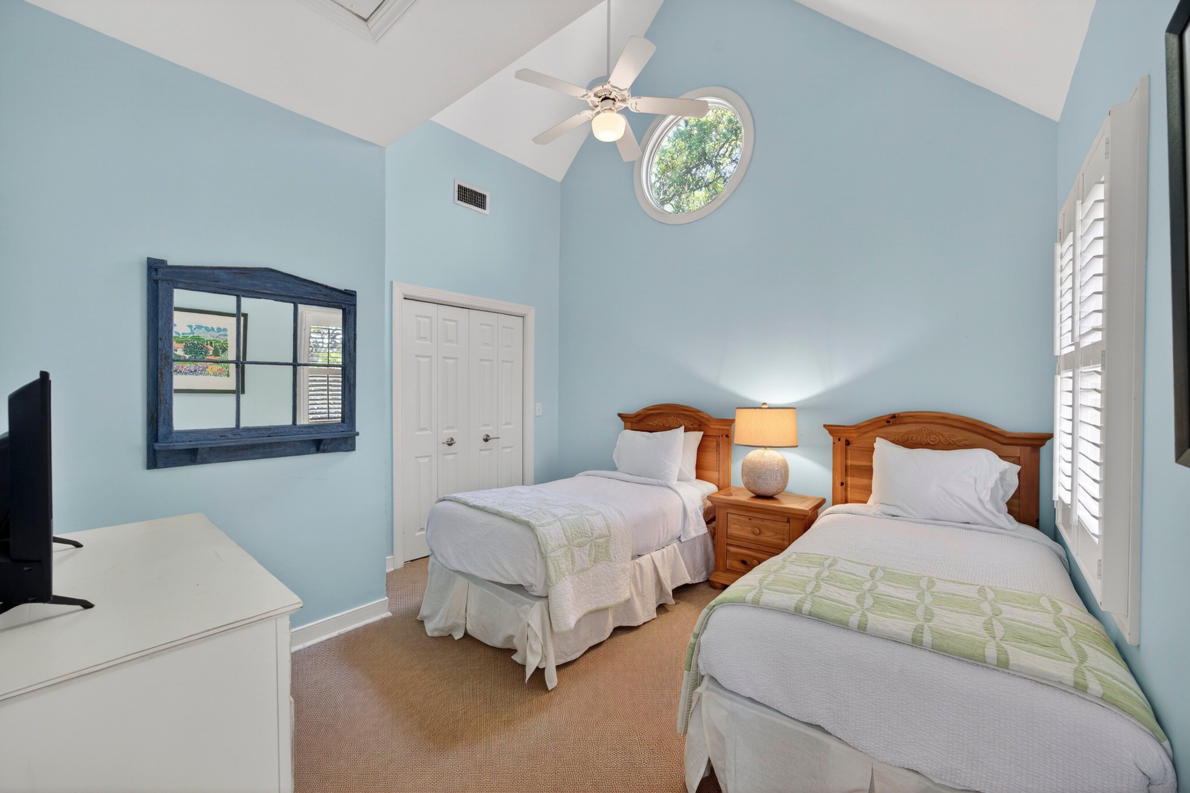 A bedroom with two beds, a ceiling fan, a window with blinds, and a desk.