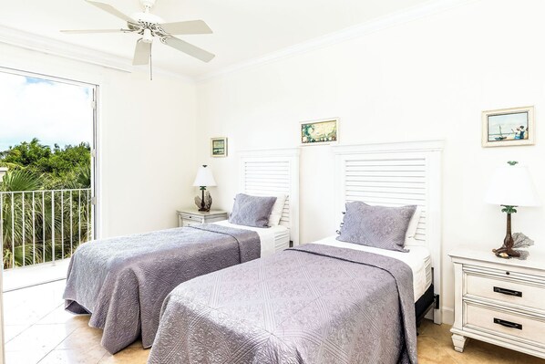 A bedroom with two beds, a balcony, and a ceiling fan.