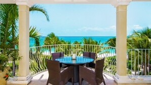 Un espace extérieur aménagé, abrité et doté de tables et de chaises, offrant une vue sur une plage bordée de palmiers et sur l’océan.
