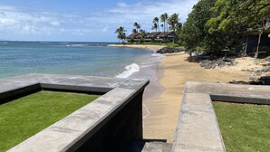 Una playa con escalones de hormigón que conducen a la orilla, palmeras y una vista despejada del océano.