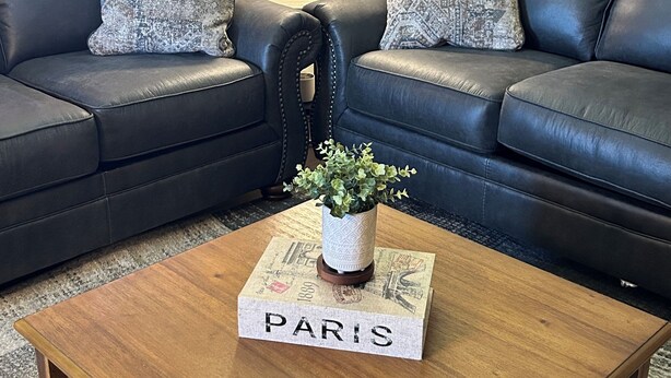 En stue med to sorte lædersofaer, et træbord med en 'PARIS' skilt, en lille potteplante og en lampe på et sofabord.