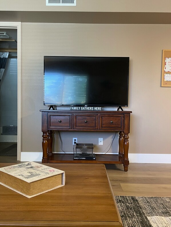 A living room with a flat-screen TV on a wooden cabinet, a coffee table, and a bookshelf.