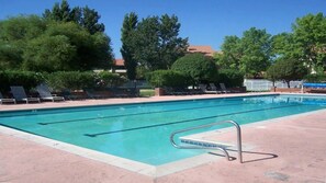 A rectangular swimming pool with clear blue water, surrounded by a tiled deck. There are lounge chairs and a metal pool ladder visible.