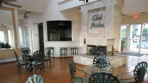 A spacious lobby with a stone fireplace labeled "Club Bahia," surrounded by green chairs and a bar area.