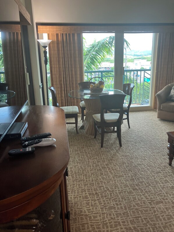 Une chambre d’hôtel dotée d’un coin repas, d’un ordinateur portable, de télécommandes et offrant une vue sur un balcon agrémenté de verdure.