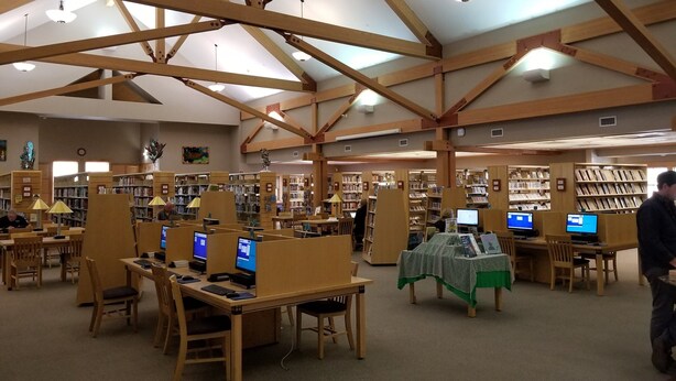 Una biblioteca con vigas de madera, varias estaciones de computadoras y estanterías.