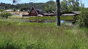 Un granero rojo con techo a dos aguas, rodeado por un campo de hierba y un pequeño estanque.