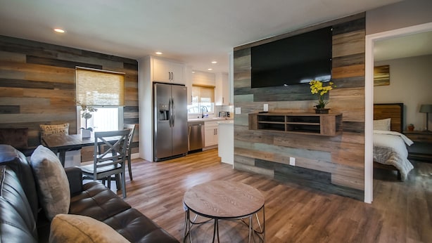Een moderne woonkamer met een leren bank, een ronde salontafel en een eethoek met een houten tafel en stoelen. Achtergrond toont een keuken met een koelkast en een flatscreen televisie.