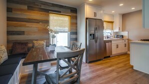 Een moderne keuken met een houten wand, roestvrijstalen apparatuur en een eethoek met een houten tafel en stoelen.