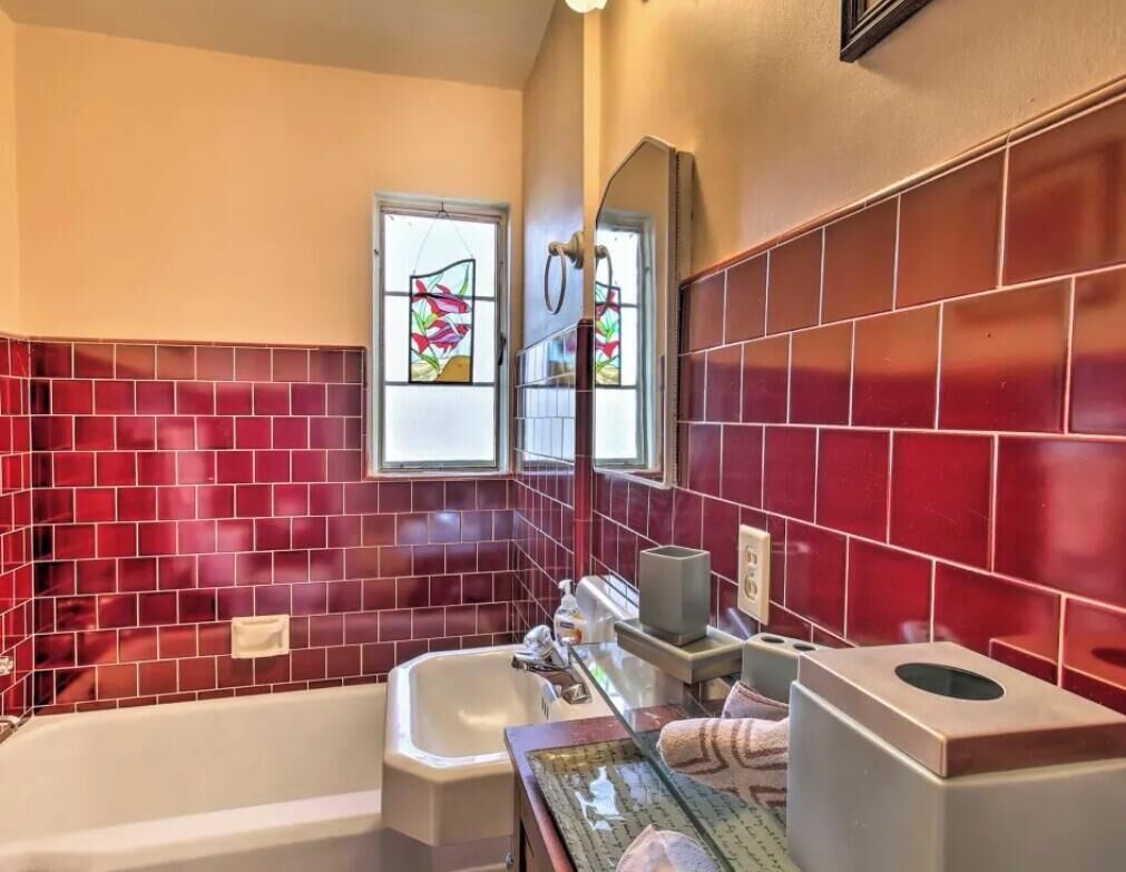A bathroom with red-tiled walls, a bathtub, a sink, and a window with stained glass.