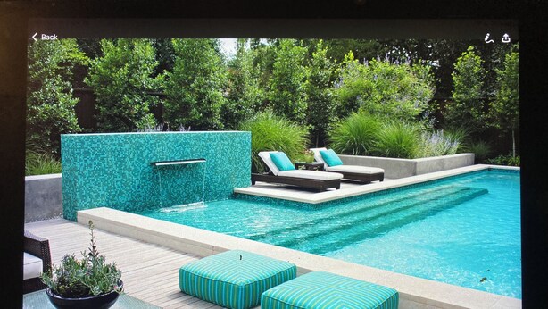 Ein moderner Poolbereich im Freien mit einer gefliesten Wand, Liegestühlen und einer Holzterrasse.