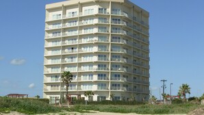 A multi-story hotel with balconies, located near a beach.