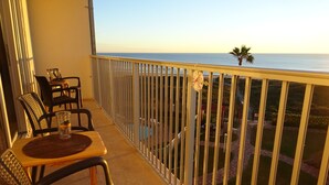 A balcony with a table and chairs, overlooking a pool and a view of the ocean.