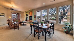 A spacious living room with a fireplace, a dining area with a wooden table and chairs, and large windows offering a view of a desert landscape. - ENTRADA GATED STUNNING VIEWS Dog Friendly New Universal EV TESLA Charger    (Santa Clara)