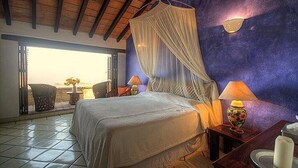 A bedroom with a bed, a nightstand, a lamp, and a view of the outdoors.