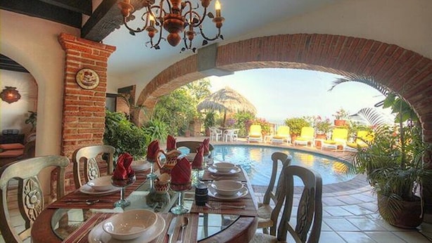 An outdoor dining area with a brick archway, a pool, and potted plants.