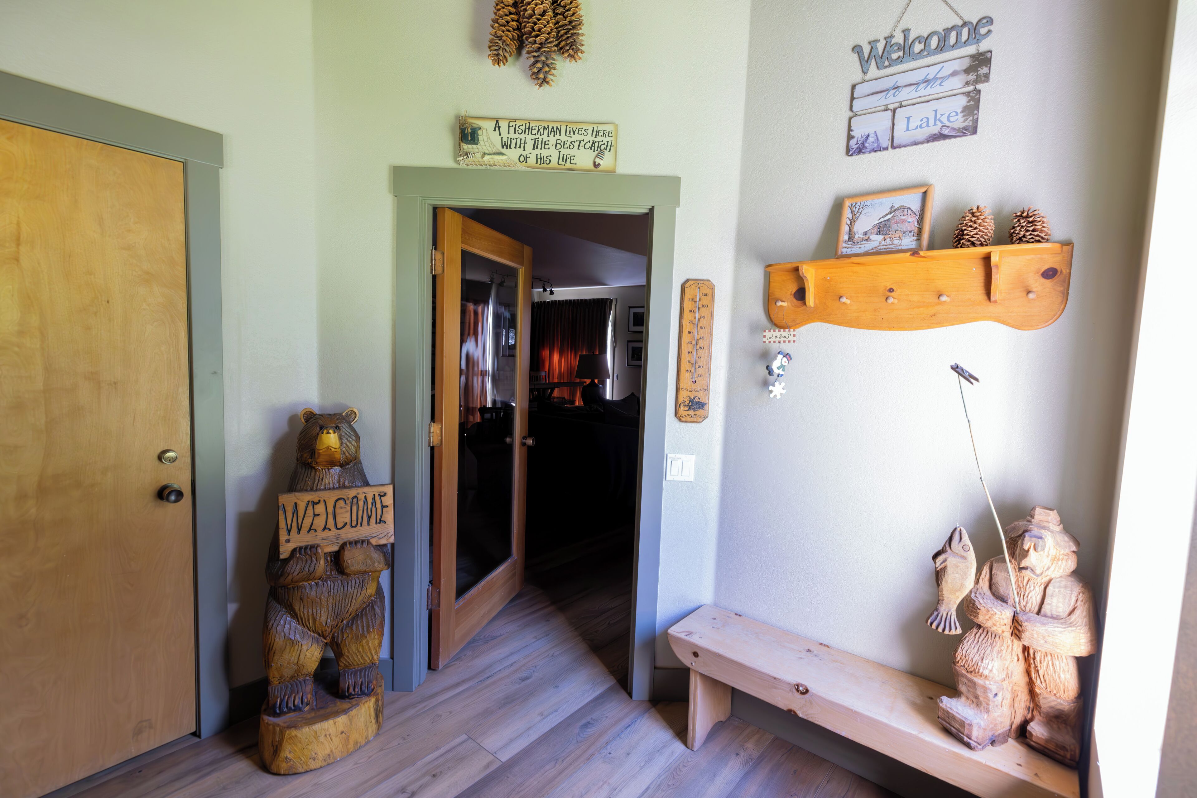 A wooden bear holding a sign, a welcome sign, and a shelf with pinecones and a fishing rod.