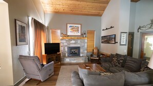 A living room with a stone fireplace, a flat-screen TV, grey sofas, and wooden flooring.