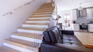 A modern interior with a staircase, a leather sofa, and a kitchen area. - Fox Den at Fox Hollow (Aldrich)