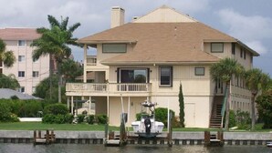 A two-story house with a balcony, a dock with a boat, and a water body in front.