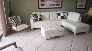 A living room with a sectional sofa, a wooden chair, and a small ottoman.
