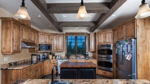 Una cocina con gabinetes de madera, encimeras de granito, electrodomésticos de acero inoxidable e iluminación colgante.
