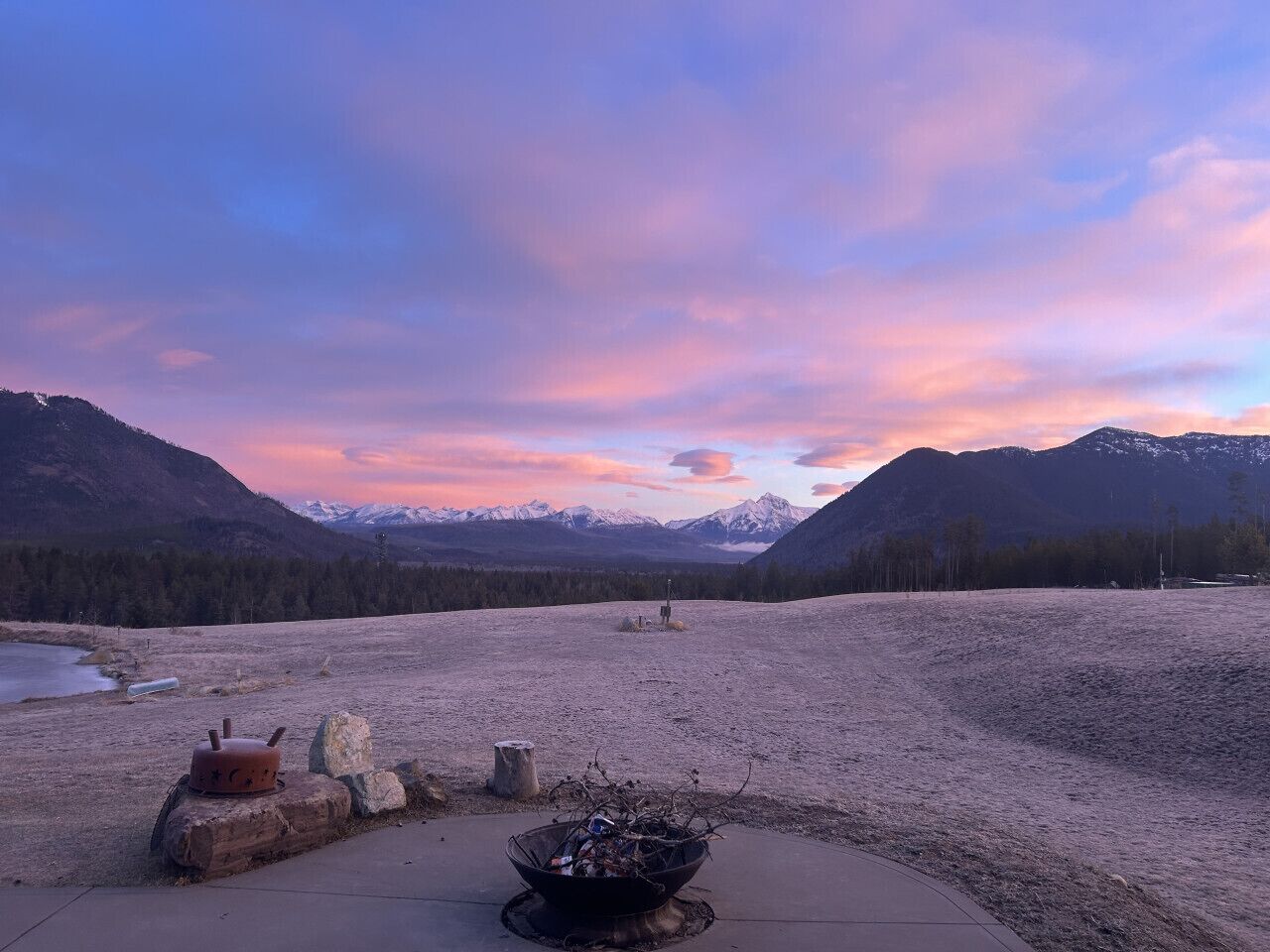 A campsite with a fire pit, a pot, and a rustic chair.