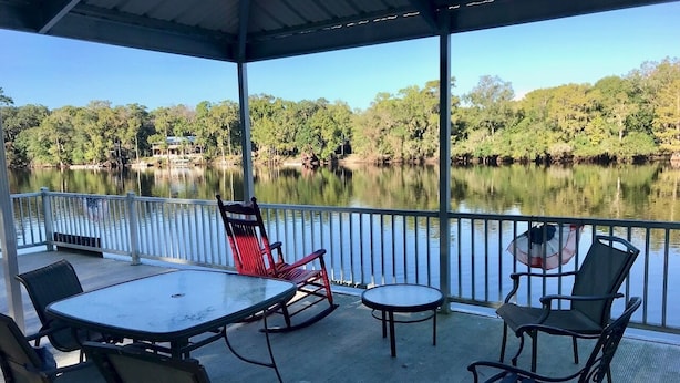 Une terrasse extérieure avec une table et des chaises, offrant une vue sur un lac paisible et une zone boisée.