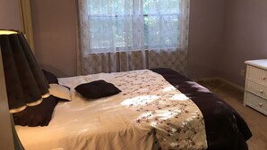 Une chambre à coucher avec un lit, une fenêtre ornée de rideaux en dentelle, une lampe de chevet et une commode.