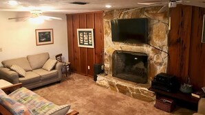 Un salon avec une cheminée en pierre, un téléviseur fixé au-dessus, un canapé et un ventilateur de plafond.