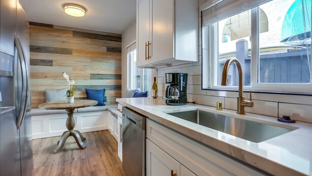 A modern kitchen with white cabinetry, a wooden accent wall, a built-in dishwasher, and a window with a view of the backyard. - Renovated Bay Side Condo - 812 (San Diego)