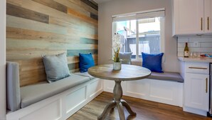 A modern kitchen with a wooden accent wall, a round dining table, and a built-in bench with blue cushions. - Renovated Bay Side Condo - 812 (San Diego)