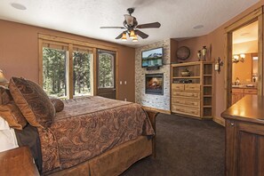 A bedroom with a bed, a ceiling fan, a fireplace, and a TV.
