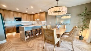 Une cuisine moderne avec des meubles en bois, un îlot central, des tabourets de bar et une table à manger avec des chaises en osier.