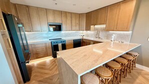 Une cuisine moderne avec des meubles en bois, un îlot central doté de tabourets, un four encastré et un réfrigérateur.