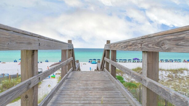 A wooden boardwalk leading to a beach with umbrellas and people. - FULLY RENOVATED 2026 BEACH VIEW - Across the street from the beach. (Destin)