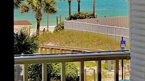 Une vue depuis un balcon donnant sur une plage bordée de palmiers, sous un ciel dégagé.
