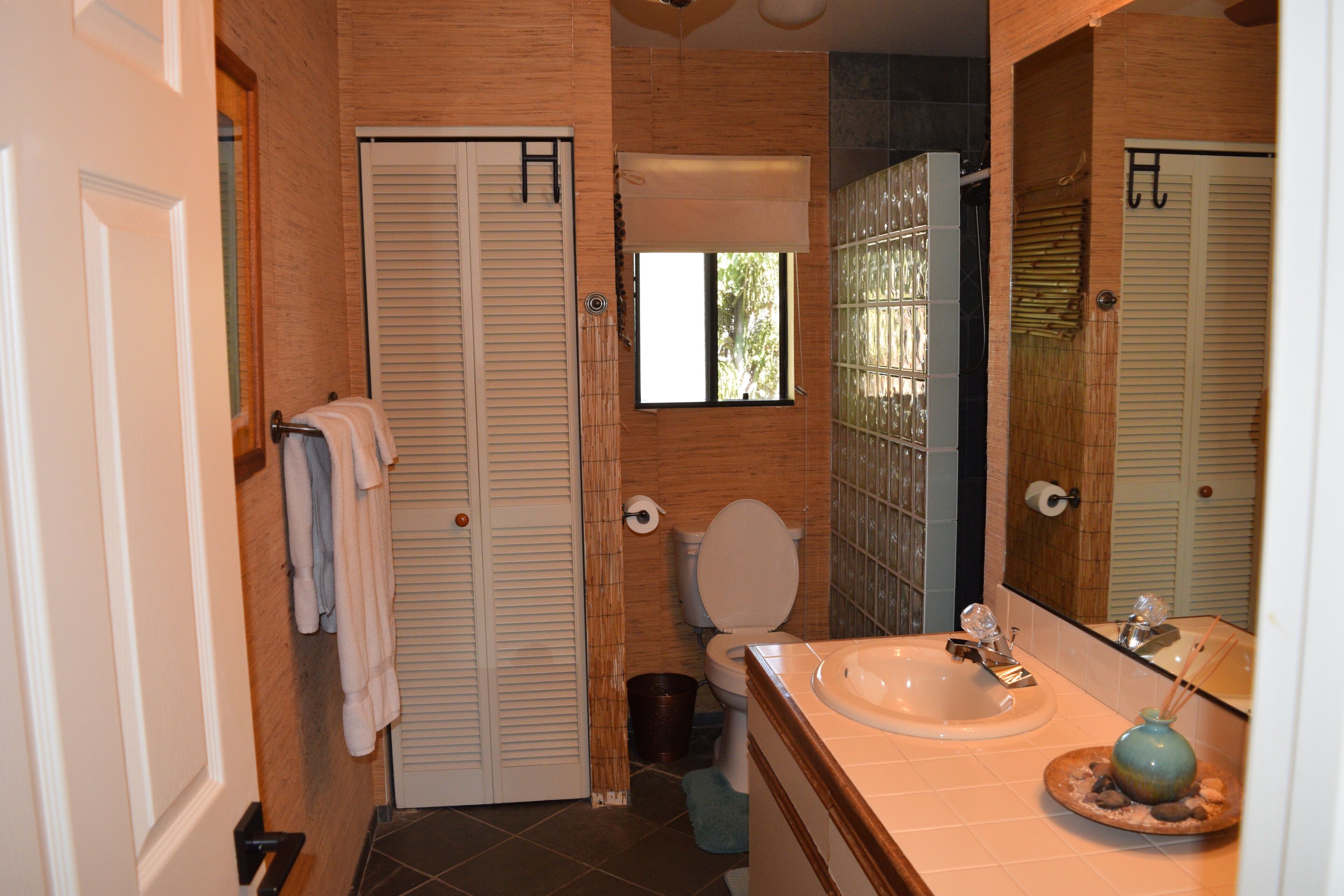A bathroom with a toilet, sink, and a mirror. There are towels hanging on a rack, and a trash bin is visible.