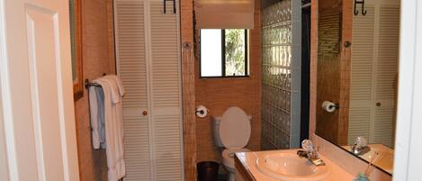 A bathroom with a toilet, sink, and a mirror. There are towels hanging on a rack, and a trash bin is visible.